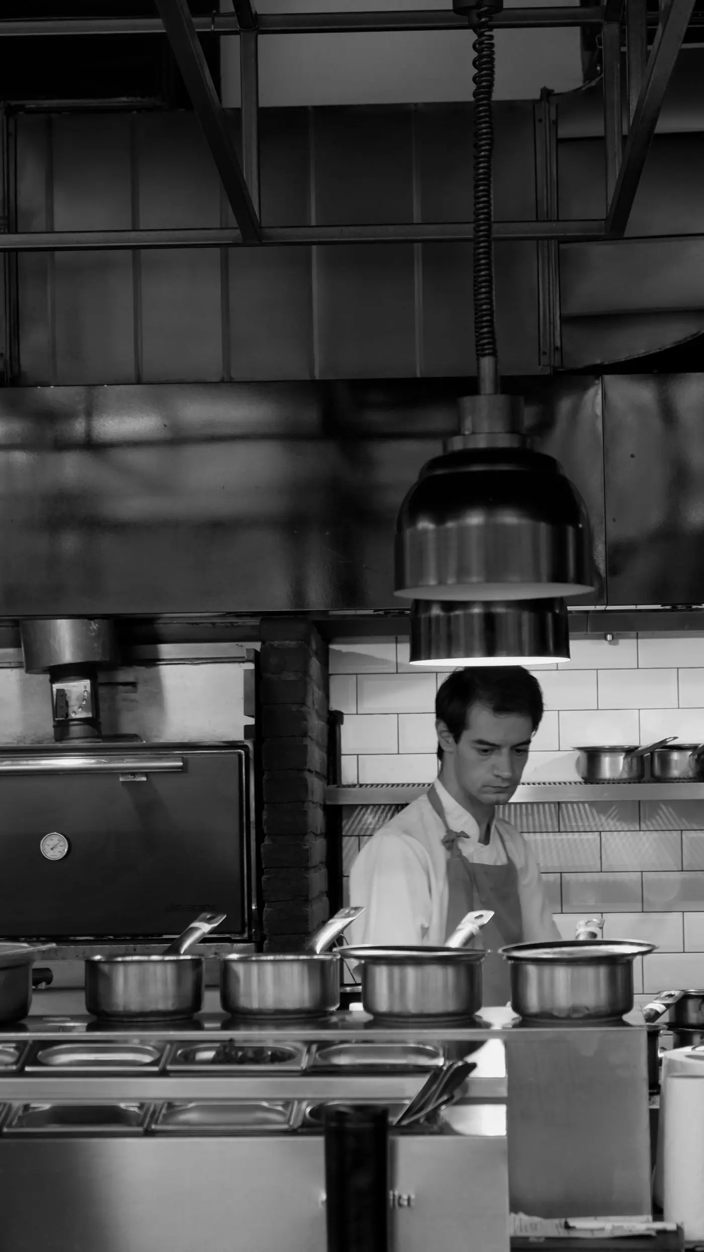 Black-and-white photo of an expediter working the pass in a restaurant kitchen.